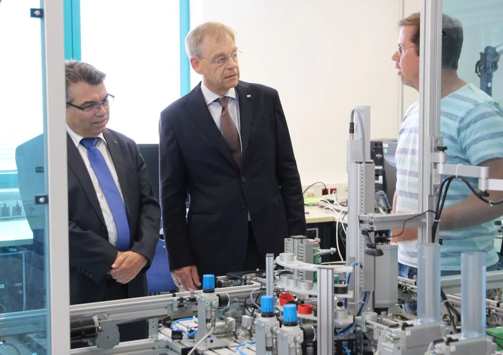 Im Labor für Steuerungstechnik erläutert Laboringenieur Matthias Loth (rechts) Eberhard Flammer (Mitte) und Prof. Matthias Willems, welche Rolle die Lernfabrik des Fachbereichs Elektro- und Informationstechnik im Studium spielt. Foto: TH Mittelhessen/Armin Eikenberg